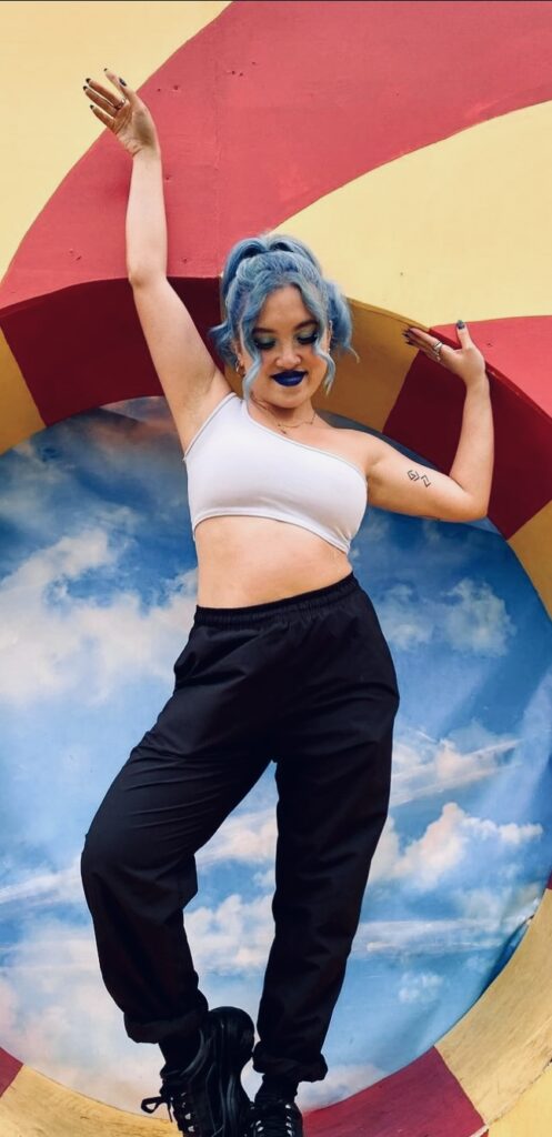 Female DJ, CHERI, is pictured posing in front of a colourful background